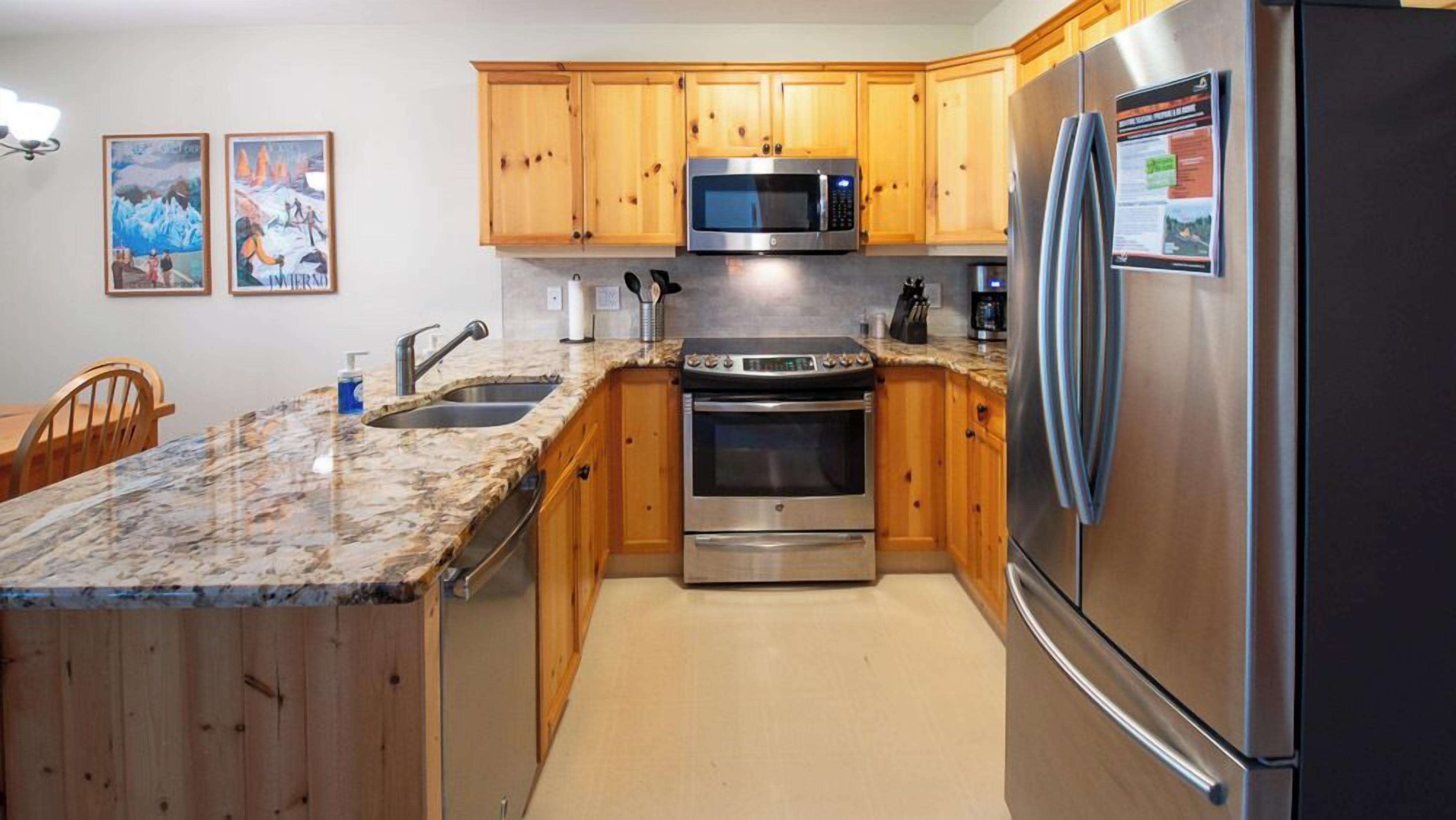 Una cocina con armarios de madera, encimera de granito y electrodomésticos de acero inoxidable, incluyendo un refrigerador, microondas y horno.