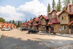 A row of wooden cabins with red roofs, arranged in a street with cars parked in front. - Stone Creek Chalet by Fernie Lodging CO (Fernie)