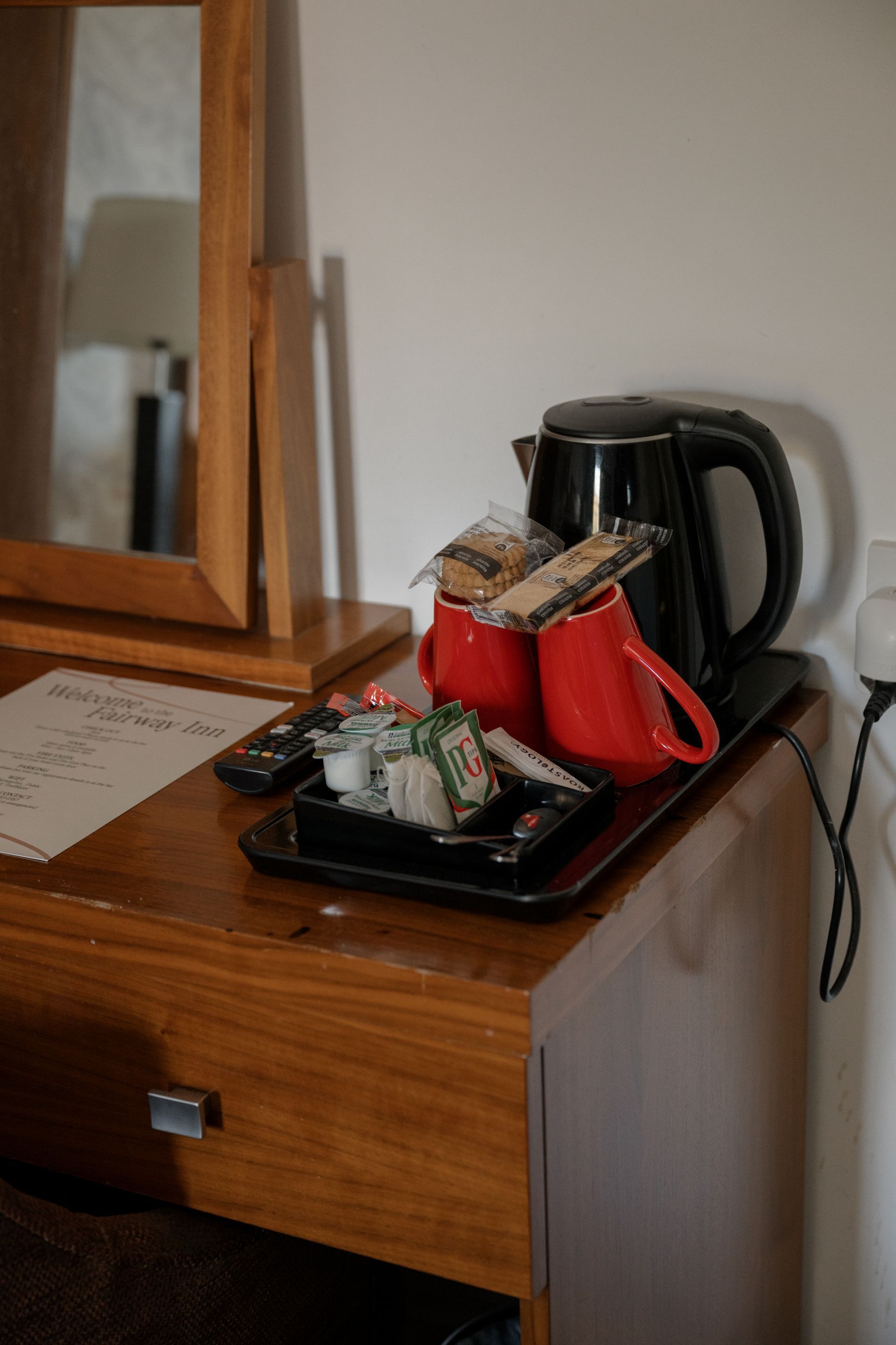 Ein Hotel-Schreibtisch mit Kaffeemaschine, roter Tasse, Tablett mit Snacks, Fernbedienung und Speisekarte.