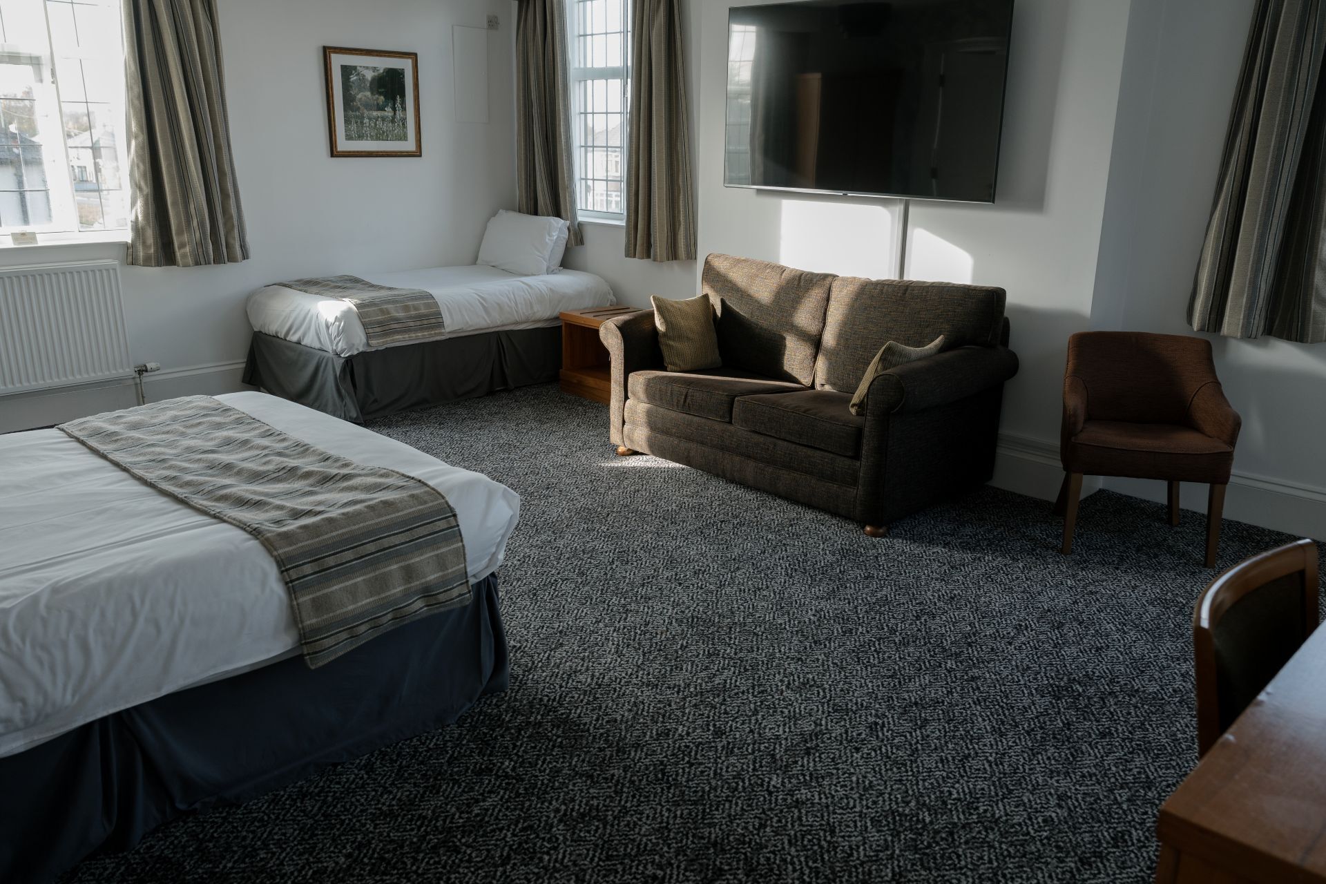 Una habitación de hotel con una cama grande, un sofá, una silla, un televisor y una alfombra estampada.