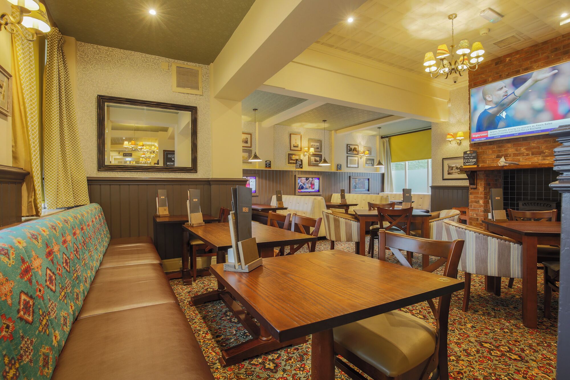 Een restaurant met zitplaatsen in hokjes, tafels en een televisiescherm.