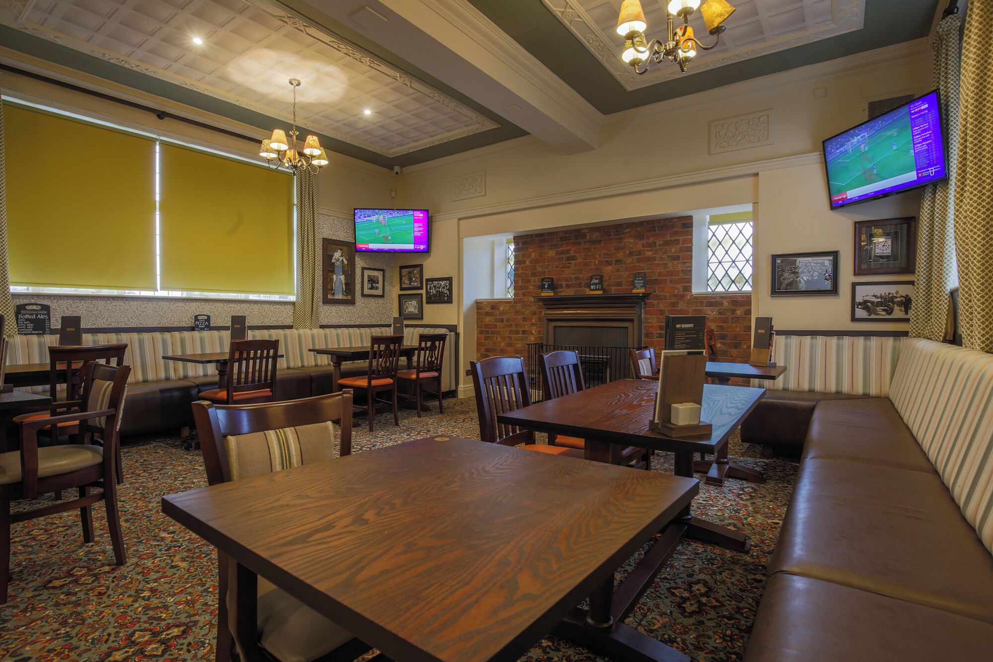 A restaurant with a brick fireplace, wooden tables and chairs, and a television screen displaying a sports game.