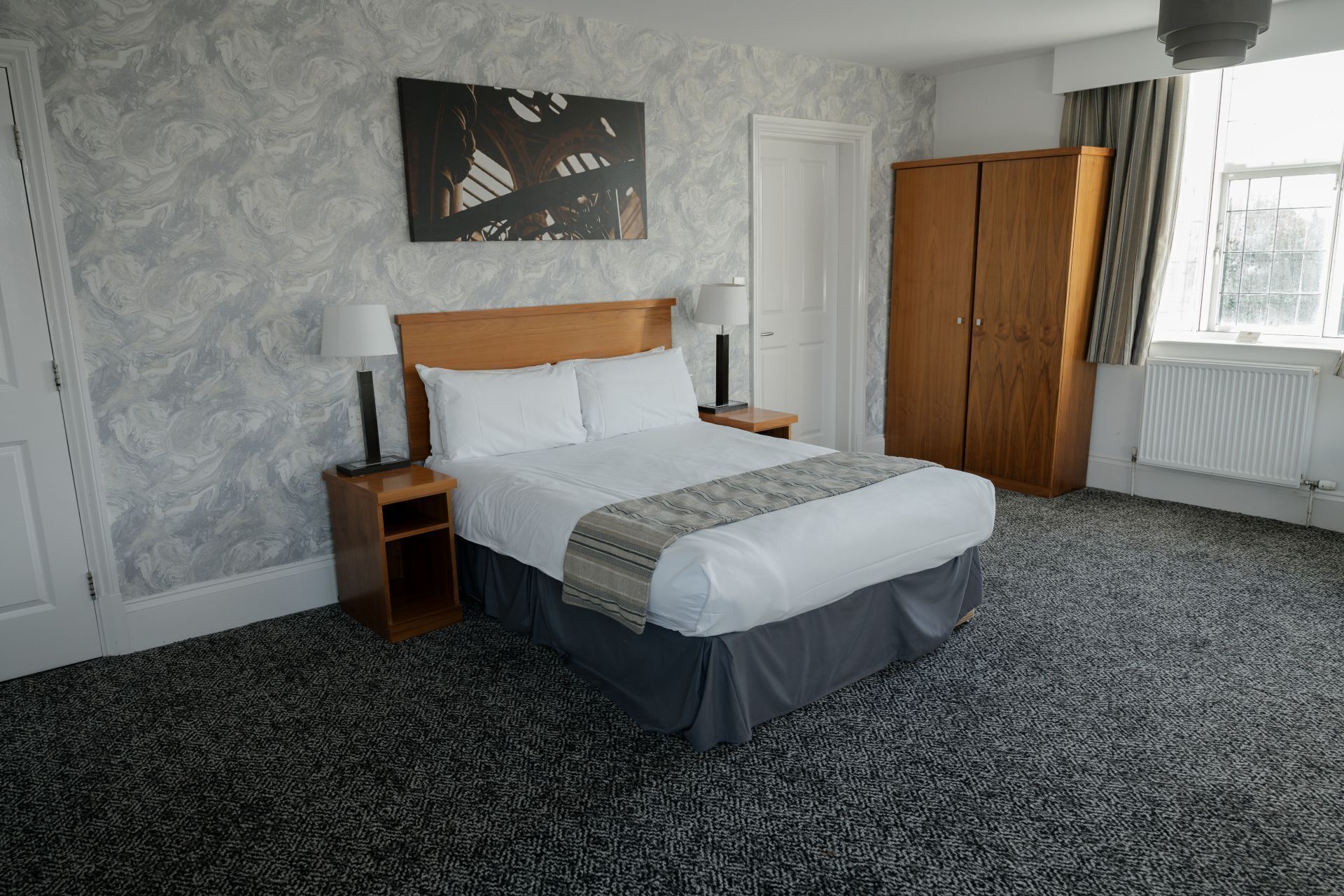 A hotel room with a bed, nightstands, a wardrobe, and a painting on the wall.