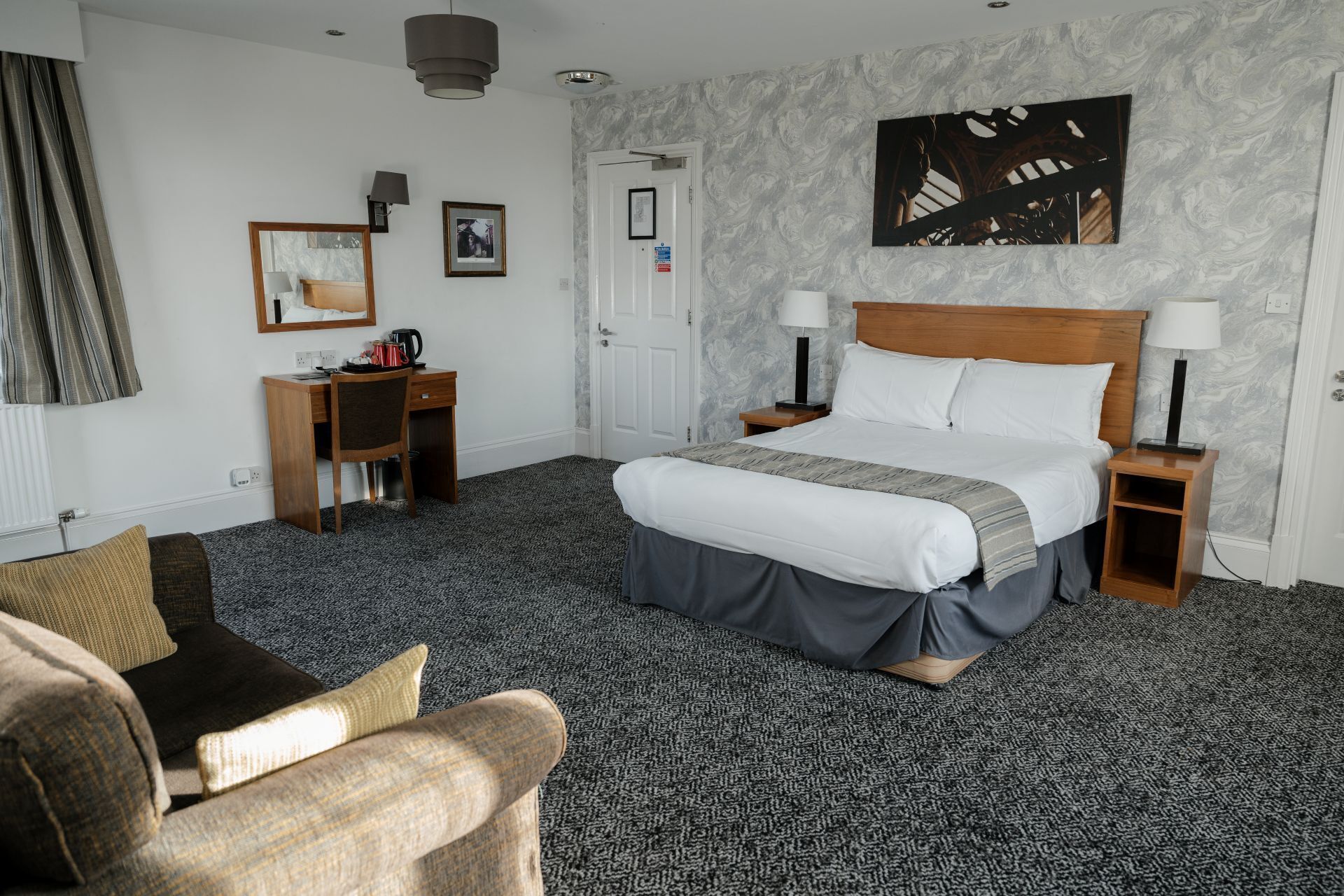 Una habitación de hotel con una cama grande, dos mesitas de noche, un escritorio con una silla, un sofá y un amplio ventanal.