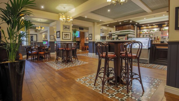 Un grand espace bar avec des tabourets hauts et un comptoir, une salle à manger avec des tables et des chaises en bois, et une cuisine dotée d’un présentoir.