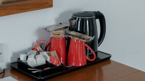 Un bureau en bois sur lequel se trouve un plateau contenant une tasse rouge, une cafetière noire et un récipient blanc. On peut également apercevoir une télécommande et une carte de bienvenue.