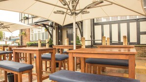 Un espace extérieur aménagé avec des tables et des bancs en bois, de grands parasols et un mur de briques en arrière-plan.