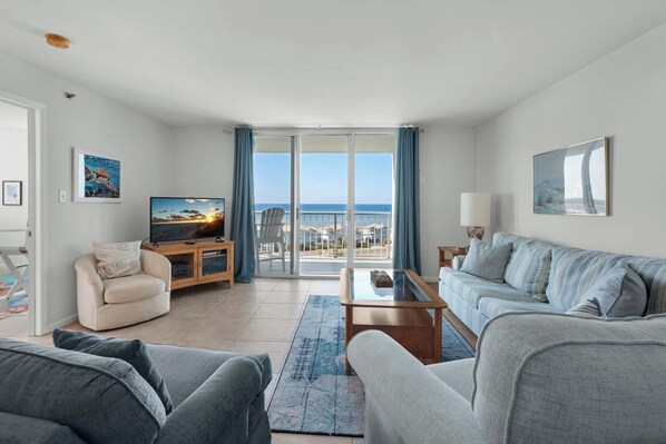 A modern living room with a large TV, a sofa set, a coffee table, and a view of the sea through large windows. - 🏝️ Bay Views | Walk to Beach☀️Tristan Towers unit 8C (Pensacola Beach)