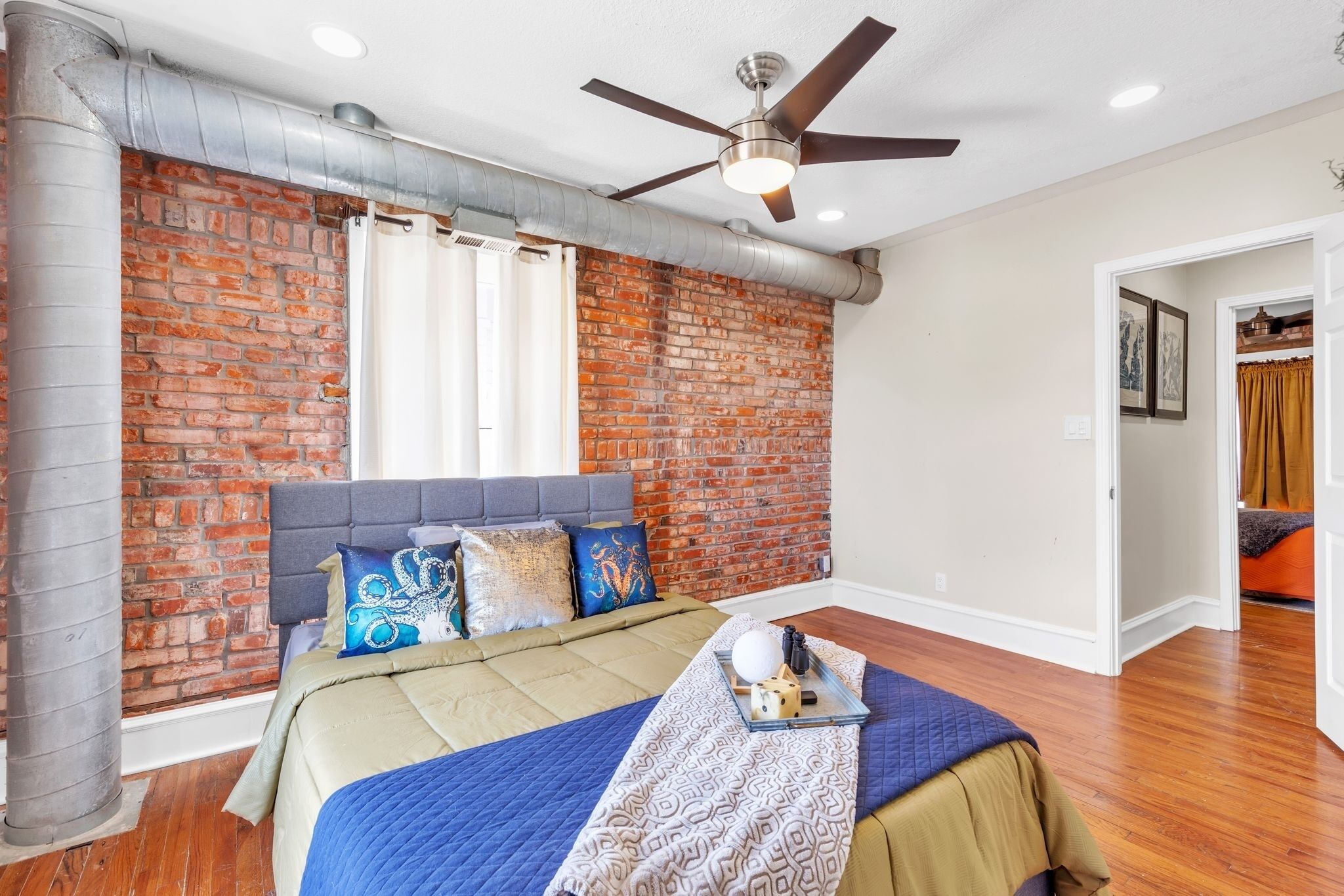 A bedroom with a brick wall, a bed with a headboard, a ceiling fan, and a window with blinds.