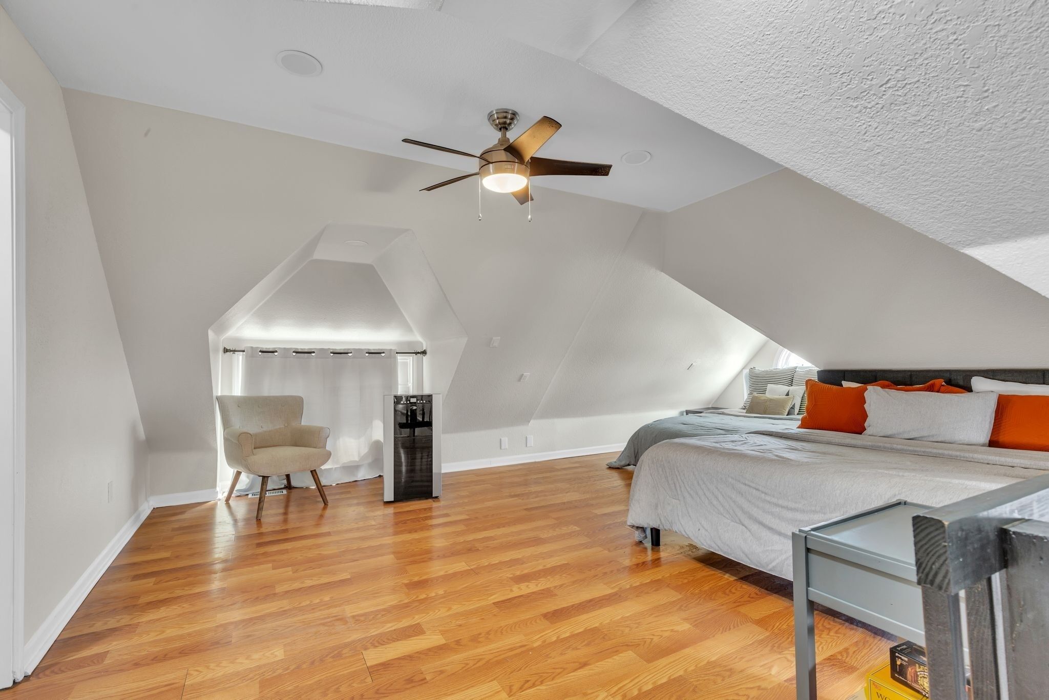 A bedroom with a sloped ceiling, a bed with pillows, a chair, and a ceiling fan.