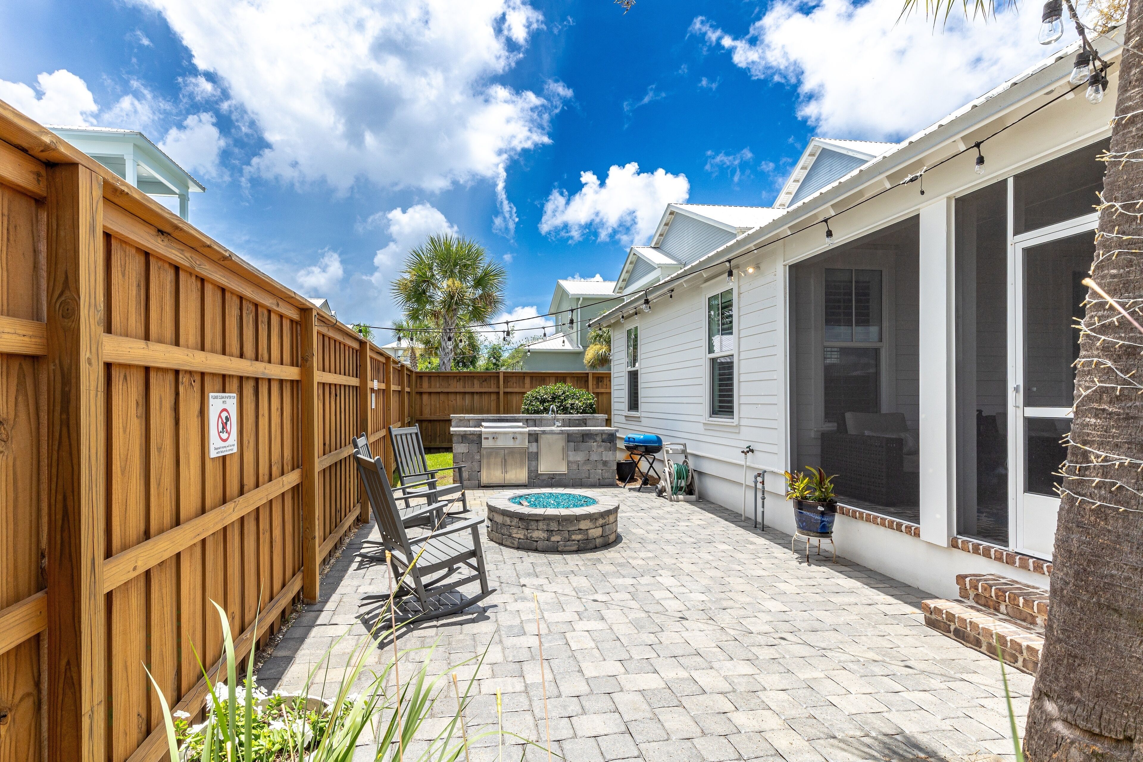 A backyard with a wooden fence, a fire pit, outdoor seating, and a house with a screened porch.