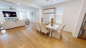 A spacious living room with a large TV, a dining area with a table and chairs, and a kitchen with a refrigerator. - Seaside Serenity 5 Bedroom Home (Miramar Beach)