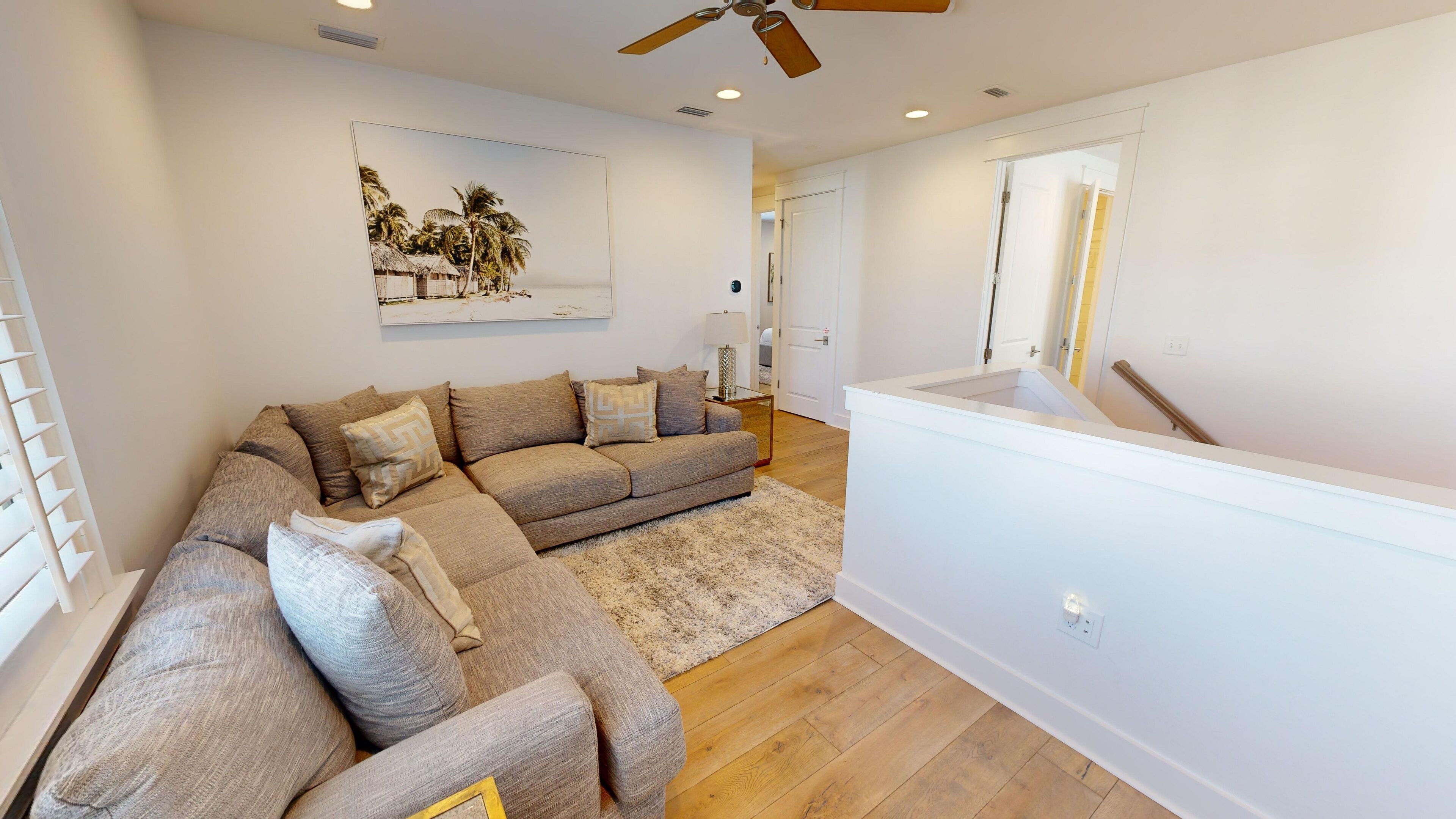 A modern living room with a sectional sofa, a small rug, and a ceiling fan.