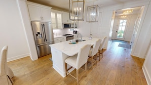 A modern kitchen with white cabinetry, stainless steel appliances, and a central island with bar stools. - Seaside Serenity 5 Bedroom Home (Miramar Beach)