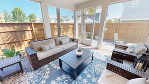 A covered patio with a wicker sofa, a coffee table, and wicker chairs. - Seaside Serenity 5 Bedroom Home (Miramar Beach)