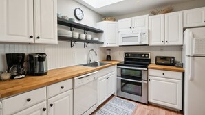 Una cocina moderna con armarios blancos, encimera de madera, horno empotrado, microondas y cafetera.