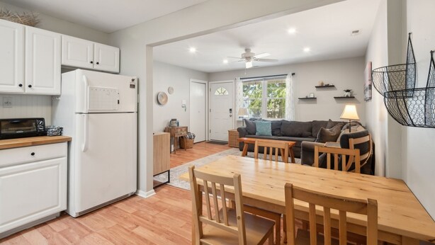 Una cocina moderna con armarios blancos, un refrigerador y un microondas. Hay una zona de comedor con una mesa y sillas de madera.