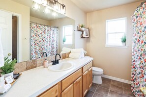 A bathroom with a white sink, wooden cabinets, a mirror, and a shower curtain with a floral pattern. - Cozy Corner Oasis With Hot Tub 4 Bedroom Home (Twin Falls)
