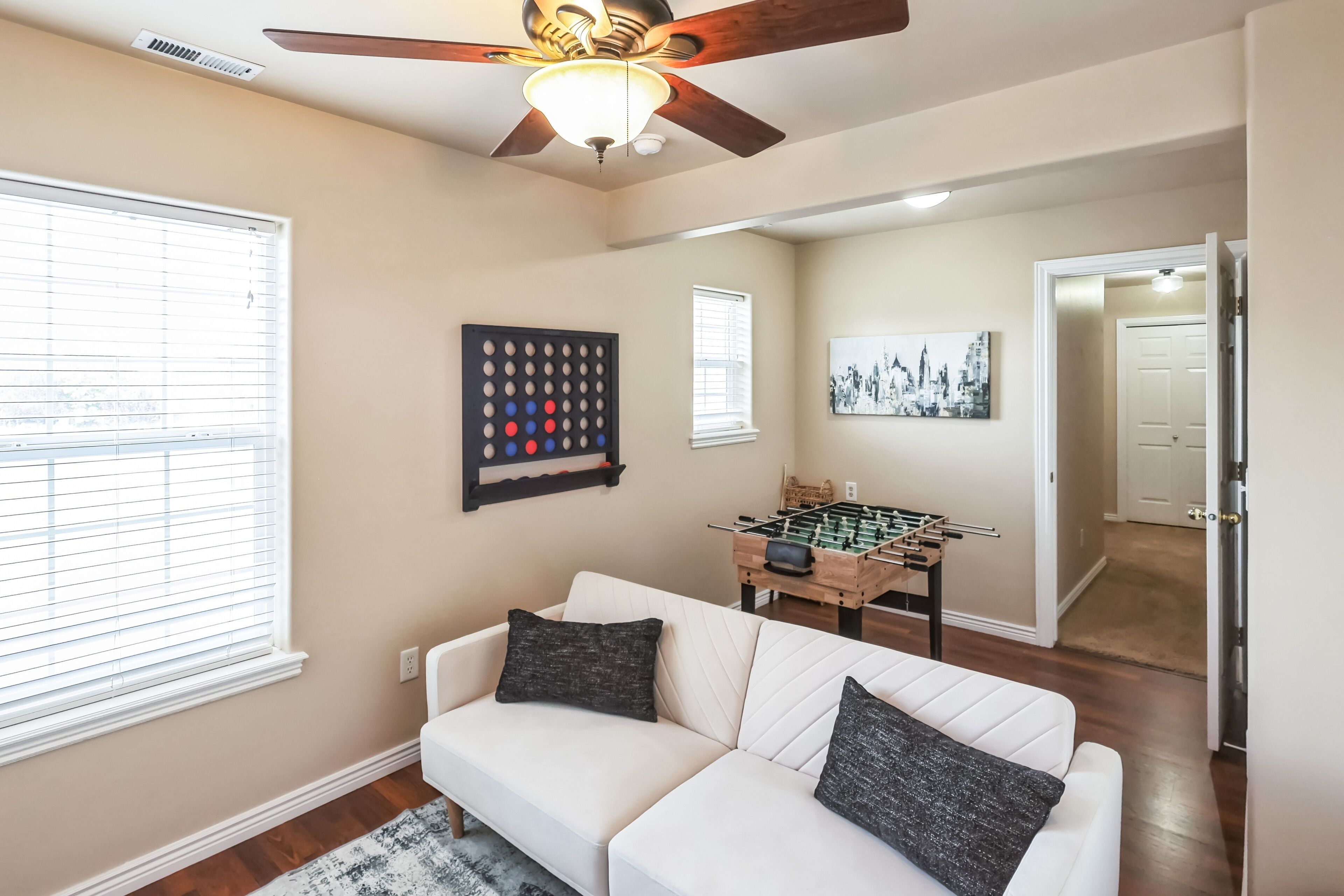 A living room with a white sofa, a foosball table, and a ceiling fan.