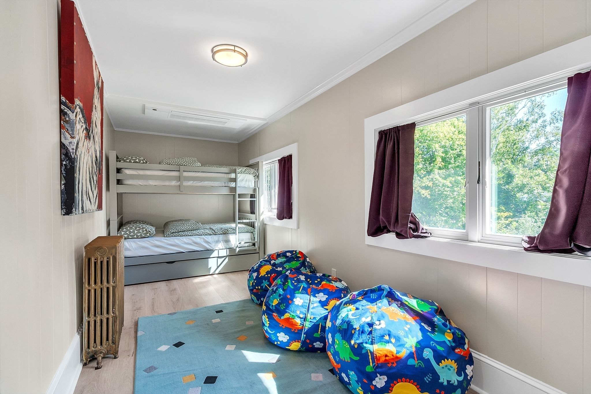 Une chambre d’enfant avec des lits superposés, des fauteuils poire, un radiateur et une fenêtre avec des rideaux.