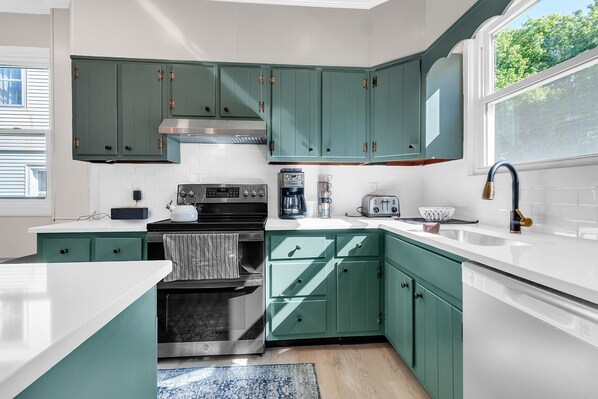 Une cuisine avec des armoires de couleur turquoise, une hotte de cuisinière en acier inoxydable, un four encastré, une machine à café et un grille-pain.