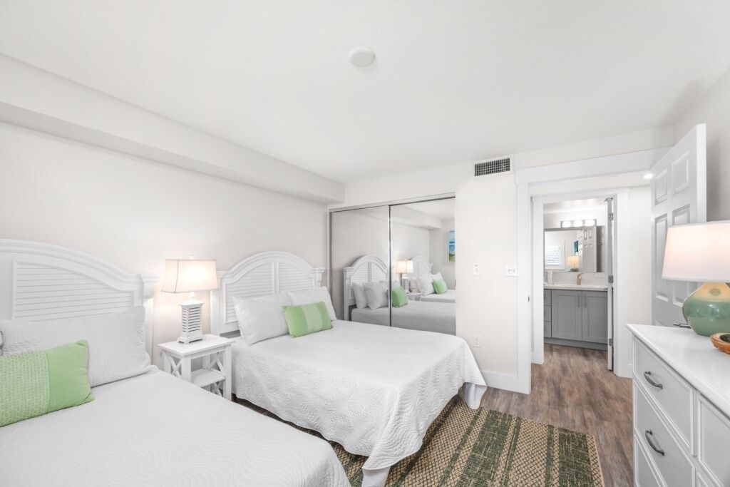 A modern hotel room with two beds, a walk-in closet, and a bathroom visible through a glass door.
