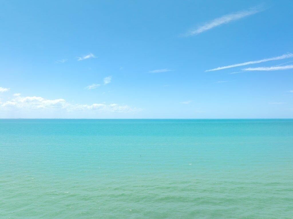 A clear view of a calm sea under a bright blue sky with a few clouds.
