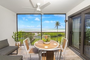 A balcony with a table and chairs, a ceiling fan, and a view of the ocean.