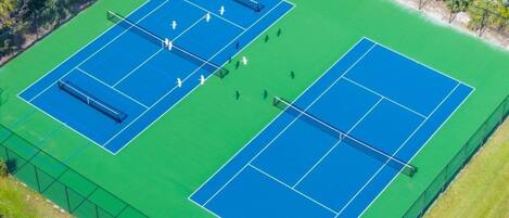 An aerial view of a tennis court complex with two courts, surrounded by a fence and palm trees.