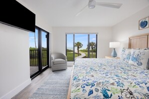 Une chambre avec un grand lit, une chaise, une table de chevet, une lampe et une vue sur l’extérieur grâce à une porte coulissante.