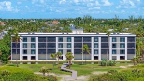 A modern building with multiple floors, surrounded by greenery and a sandy area. - Pelicans Roost 104 2 Bedroom Condo (Sanibel)
