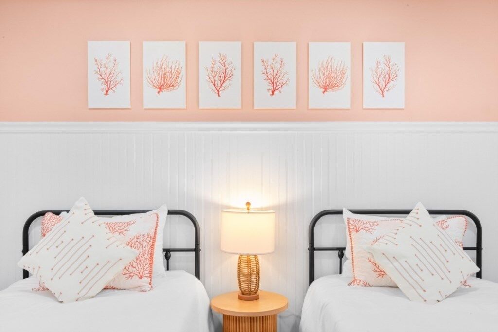 A bedroom with two beds, a bedside table with a lamp, and five wall-mounted pictures.