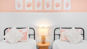 A bedroom with two beds, a bedside table with a lamp, and five wall-mounted pictures. - Tarpon Beach 302 3 Bedroom Condo (Sanibel)