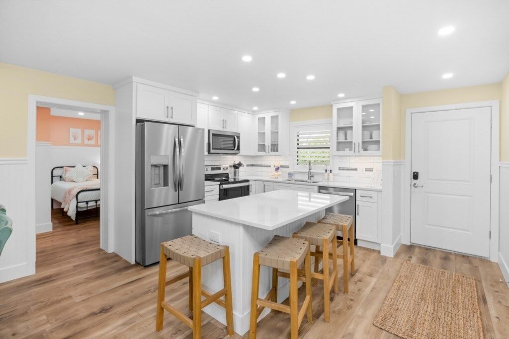 A modern kitchen with white cabinets, stainless steel appliances, and a central island with stools.