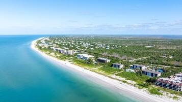 An aerial view of a coastal area with a beach, buildings, and greenery.