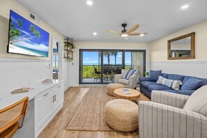 A living room with a TV, sofas, a coffee table, and a view of the outdoors. - Tarpon Beach 302 3 Bedroom Condo (Sanibel)