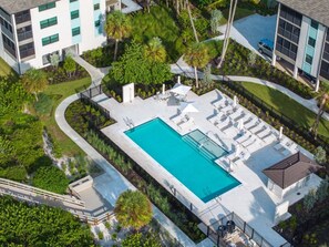 An aerial view of a modern building with a rectangular swimming pool surrounded by lounge chairs and a covered seating area. - Tarpon Beach 302 3 Bedroom Condo (Sanibel)