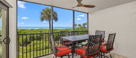 A balcony with a table and chairs, a ceiling fan, and a view of the ocean.