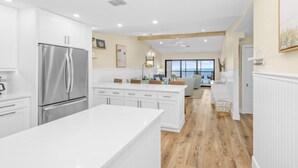 A modern kitchen with white cabinetry, a stainless steel refrigerator, and a large island. - Tarpon Beach Unit 110 2 Bedroom Condo (Sanibel)