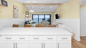 A modern kitchen with white cabinetry, a large island, and a dining area with a view to the outside. - Tarpon Beach Unit 110 2 Bedroom Condo (Sanibel)