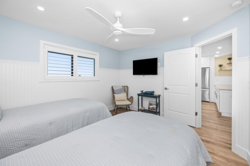 A bedroom with two beds, a ceiling fan, a TV, and a door leading to a kitchen.