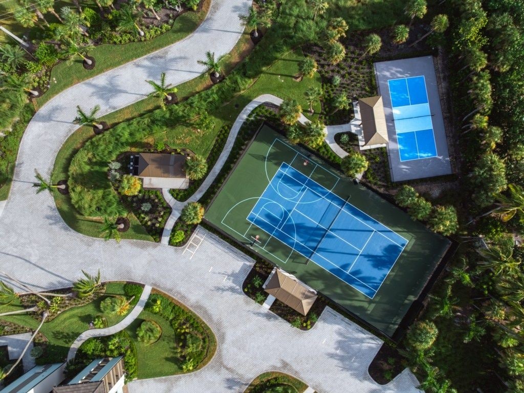 An aerial view of a property with a tennis court, landscaped gardens, and a building with a blue roof.