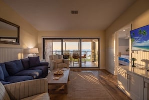 A living room with a sofa, coffee table, and a view of the balcony. - Tarpon Beach Unit 110 2 Bedroom Condo (Sanibel)