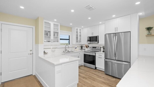 A modern kitchen with white cabinetry, stainless steel appliances, and a wooden floor. - Tarpon Beach Unit 110 2 Bedroom Condo (Sanibel)