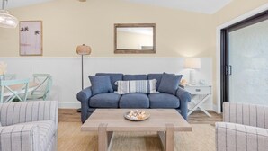 A living room with a blue sofa, a wooden coffee table, and a small side table with a lamp. - Tarpon Beach Unit 110 2 Bedroom Condo (Sanibel)