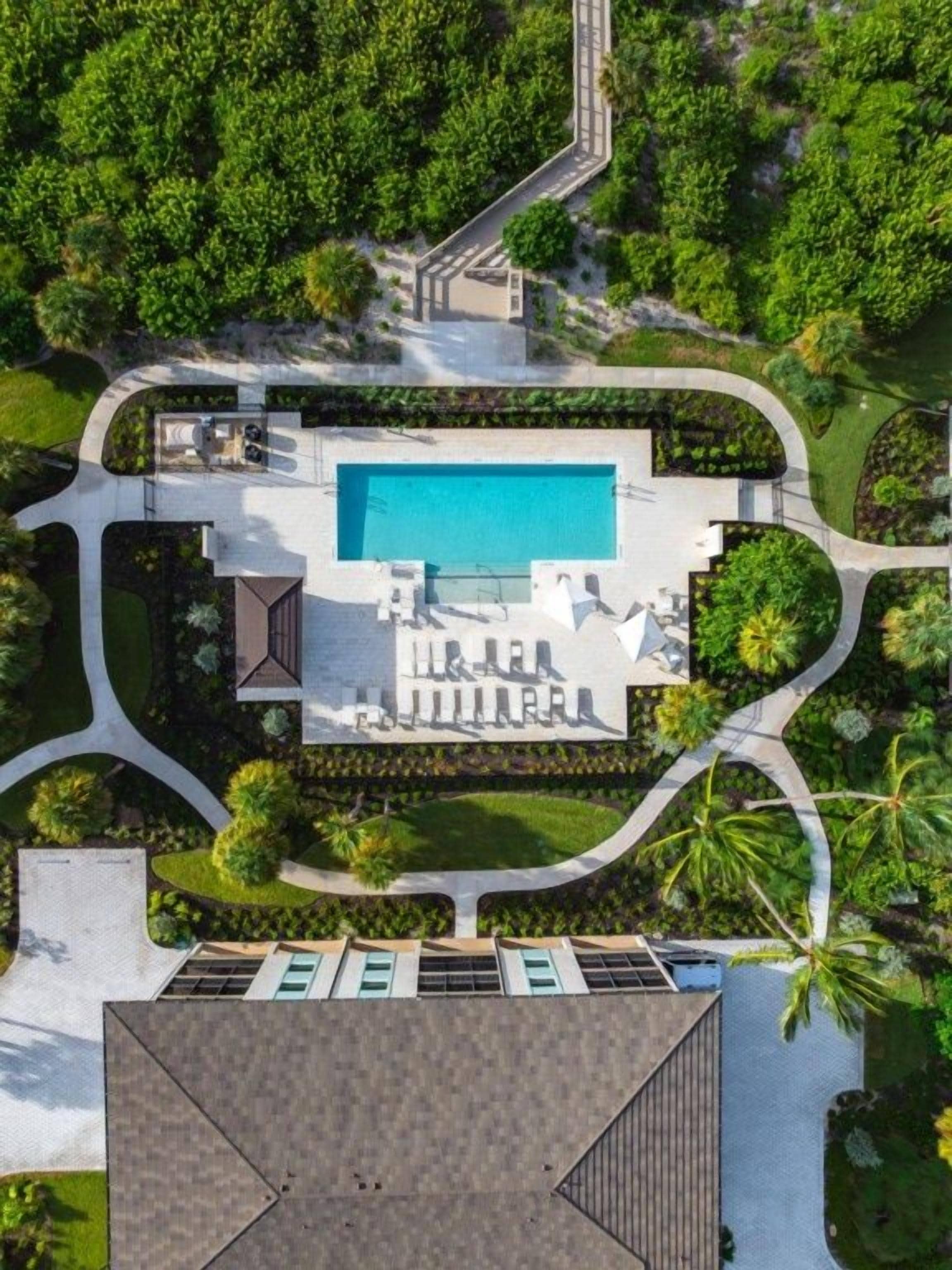 An aerial view of a resort with a swimming pool, lounge area, and landscaped gardens.