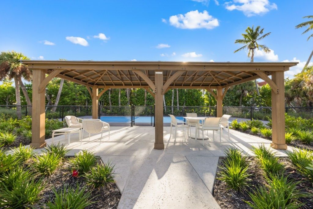 Un patio exterior con pérgola, mobiliario y una piscina.