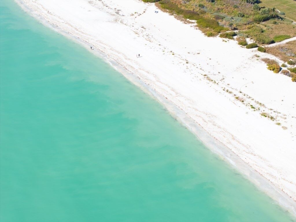 An aerial view of a beach with clear turquoise water and white sand.