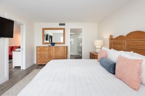 Un dormitorio con una cama grande, cabecera de madera, cómoda, espejo y televisor.