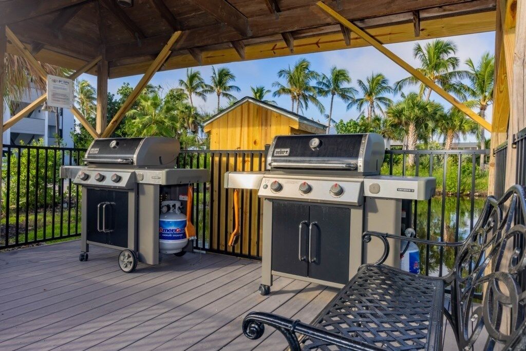 An outdoor barbecue area with two grills, a gas tank, and a covered seating area with a metal table.